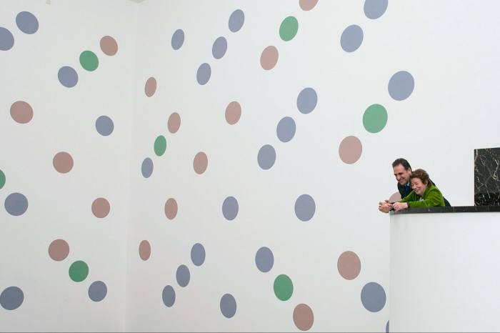 Two figures look at a large mural of green, purple and salmon-coloured polkadots