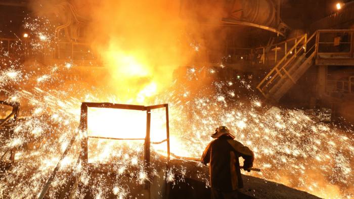 A worker supervises the flow of hot liquid metal as it flows from the blast furnace during the iron smelting process at a plant in Russia