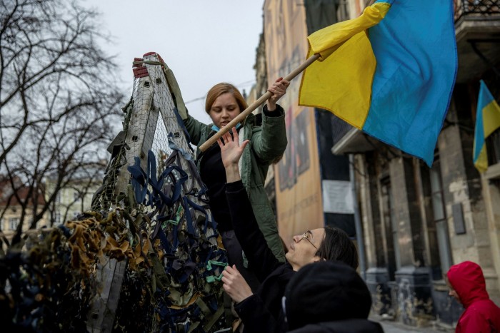 Volunteers raise a Ukrainian flag while making camouflage nets in Lviv. Ukrainians are organising into groups at a neighbourhood level to aid the war effort and help people under attack from the Russian army