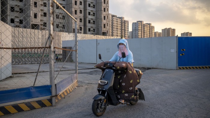 A woman rides a scooter past the China Evergrande Group Royal Peak construction project in Beijing