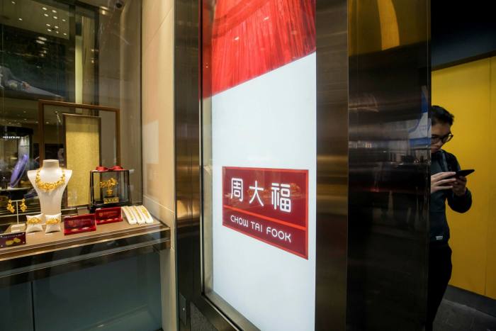 A pedestrian uses a smartphone outside a Chow Tai Fook jewellery store  