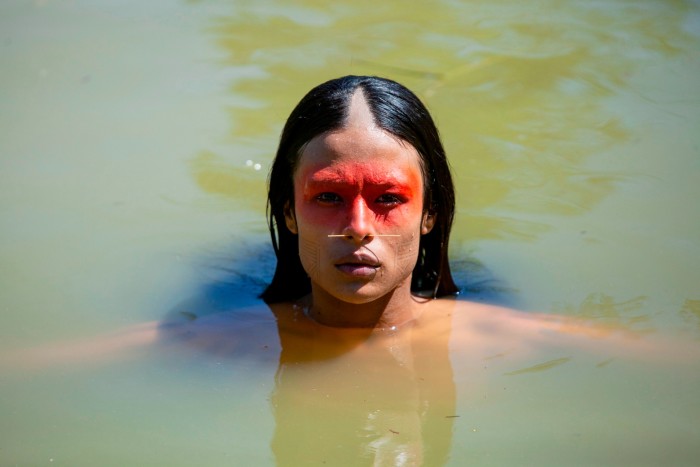 The head of a person with striking red facial marks swimming in a river 