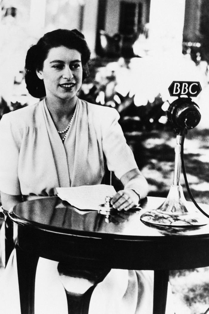 Princess Elizabeth in 1947, sits smiling at a table where there is a BBC microphone
