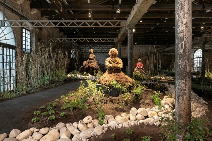 Large figures made of earth sit with their arms crossed in an indoor garden