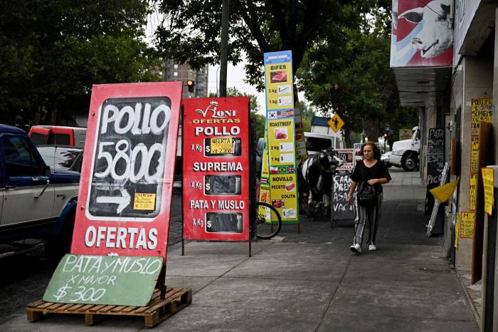 A woman walks between signs denoting food prices in a street in Buenos Aires on Thursday