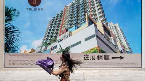 A pedestrian walks past an advertisement for the T-Plus Housing project in Hong Kong
