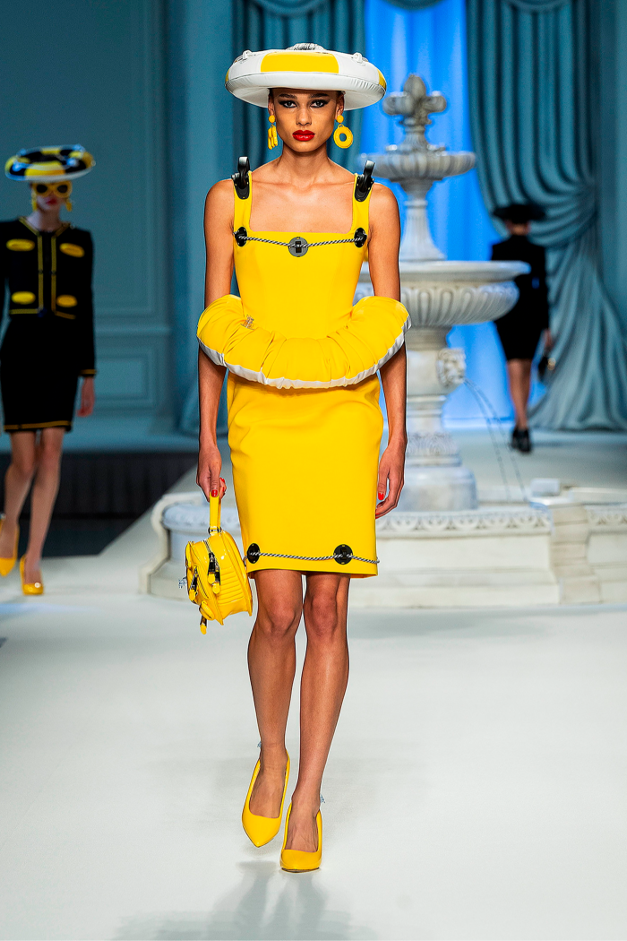 A female catwalk model in a matching yellow dress, hat, handbag and shoes