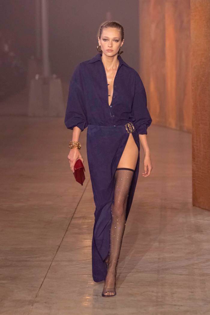 A model wears a dark blue evening gown that is split at the waist on one side