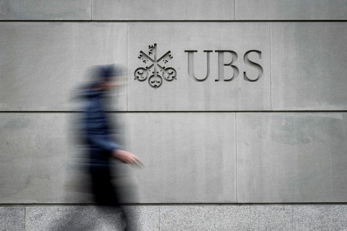 A pedestrian walks by the logo of Swiss banking giant UBS engraved on the wall of its headquarters