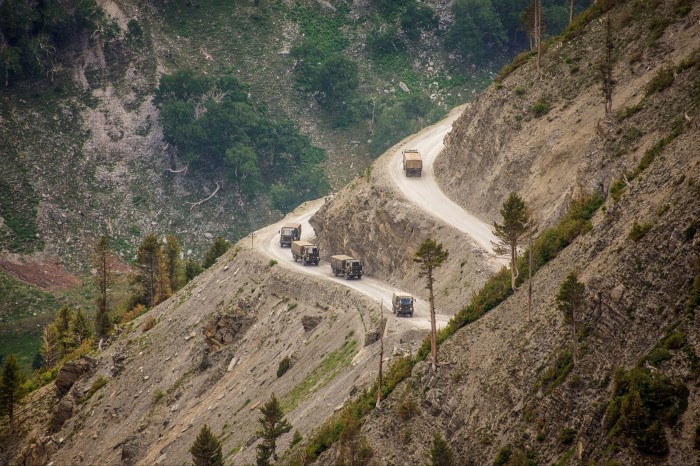 Army trucks drive along winding track towards a hill
