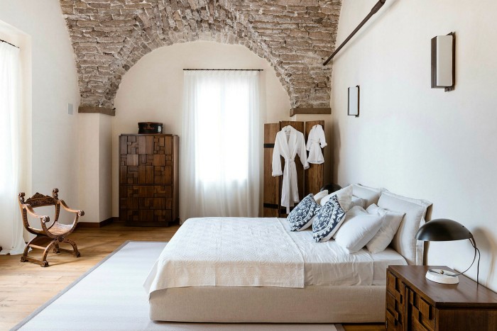 Double bed with cream coloured bedlinen in a large room with white walls and a vaulted brick ceiling