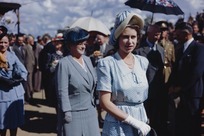 Princess Elizabeth, in summer dress, hat and gloves, smiling in the sunshine, with crowds of people behind her