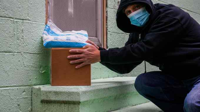 A posed photograph of a man stealing an Amazon package with other items sitting on a front door step