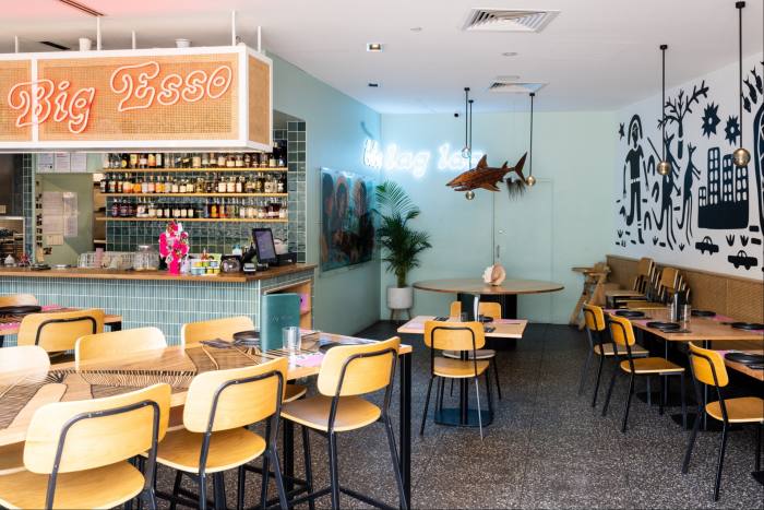 The interior of Big Esso restaurant, with seating and tables, a red neon sign above the counter saying ‘Big Esso’, a bamboo sculpture of a tiger shark and a black and white indigenous-art mural on a side wall