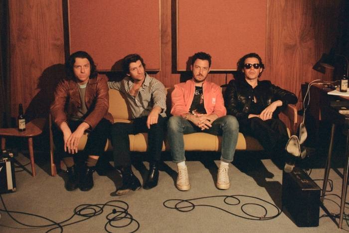 Four men in slick, expensive hipster clothes sit on a sofa in a recording studio