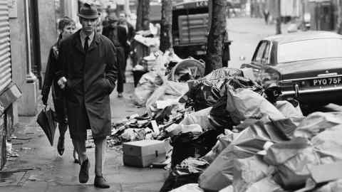 A disgruntled pedestrian walks to work amid piles of rubbish which has accumulated because of a strike by council dustmen in 1970