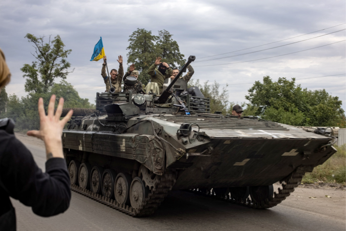 A civilian waves to Ukrainian soldiers riding on an armored personnel carrier