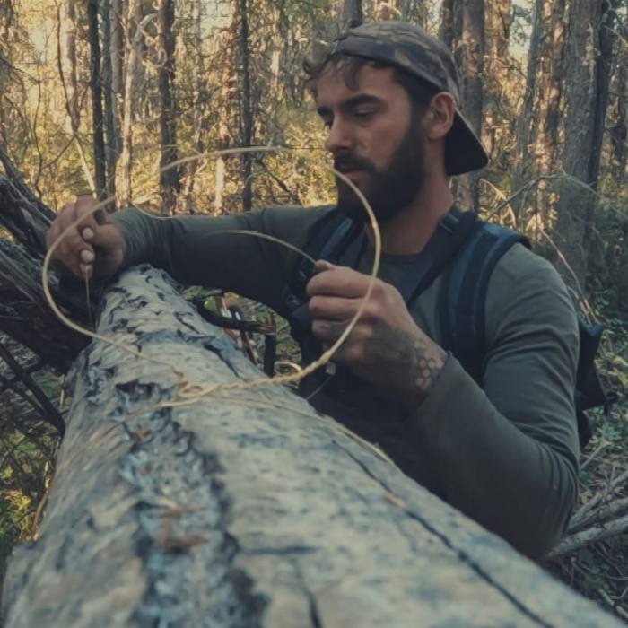 Een man gebruikt een draad om boomstammen vast te binden 