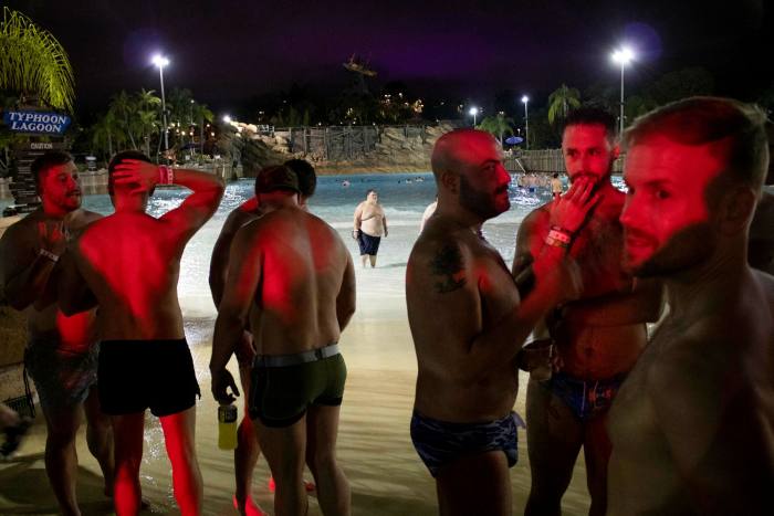 Men in swimming trunks stand by a pool at night