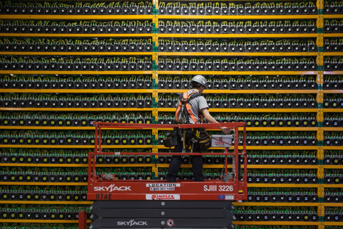 A technician stands in a cherry picker as he inspects a vast bitcoin mining array