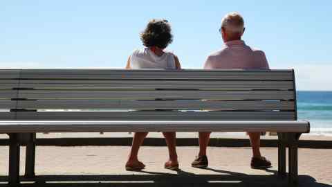 View from behind of two pensioners sitting on a bench in the sunshine in Australia, looking out sea