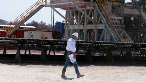 Seorang pekerja berjalan melepasi timbunan paip gerudi yang diperlukan untuk menoreh minyak dan gas di tapak penggerudian minyak Chesapeake di syal Eagle Ford berhampiran Crystal City, Texas