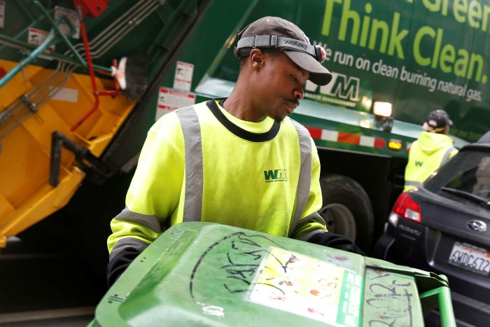A Waste Management Agency employee collects a trash can on the street in Oakland, California 