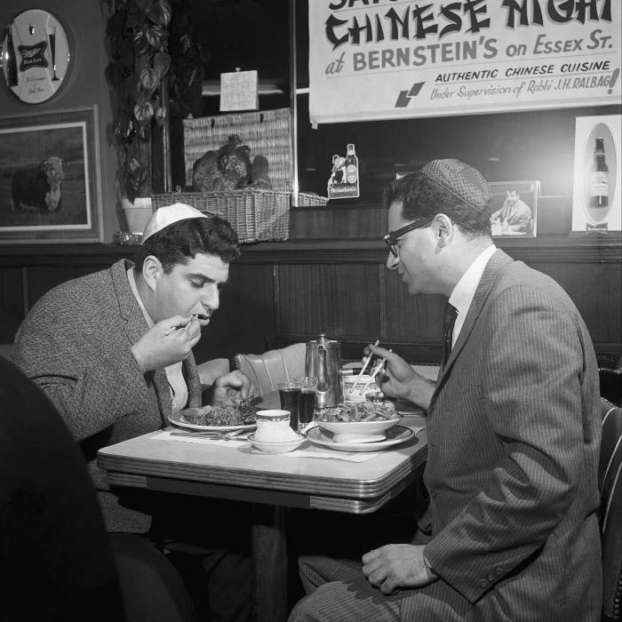 Two men wearing kippah hats eat Chinese food at a diner