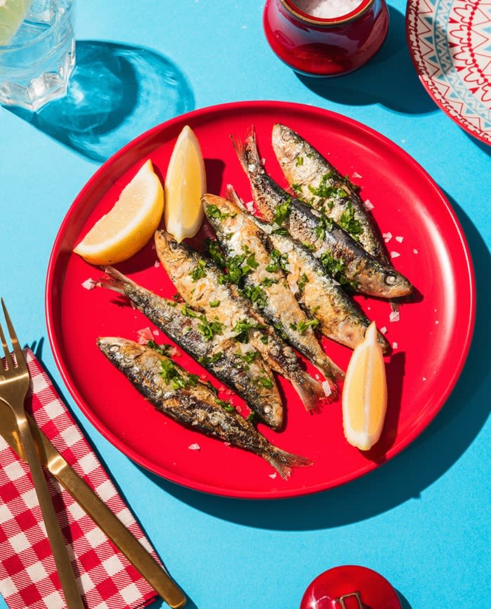 Fried sardines on a red plate with lemon wedges