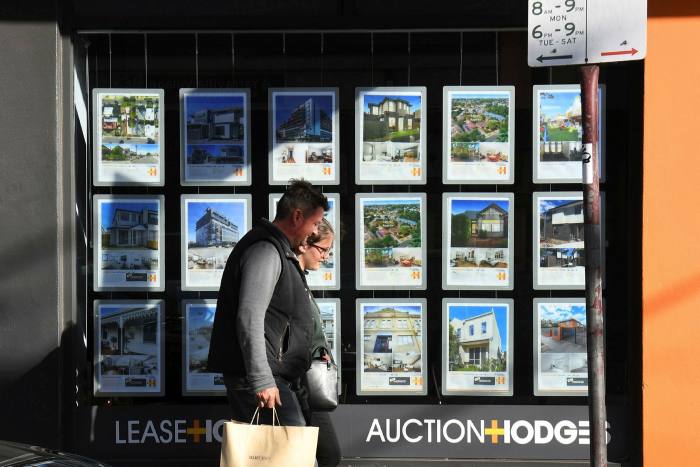 A couple walks past a real estate agent’s window advertising houses for sale and auction in Melbourne