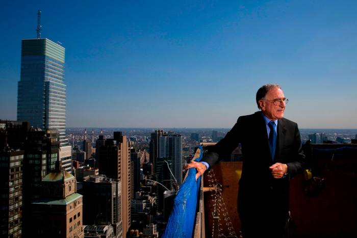 A man stands on top of a building with the New York skyline behind him