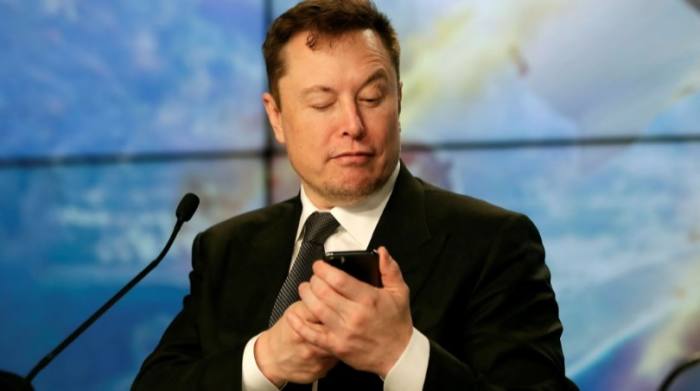 Elon Musk schaut während einer Veranstaltung auf sein Handy