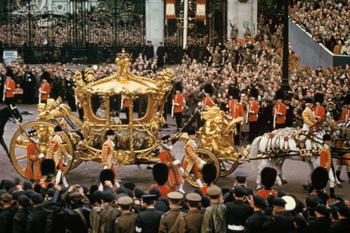 A golden carriage with footmen  on a crowded London street