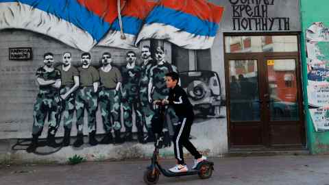 A boy on a scooter goes past a Serb nationalist mural