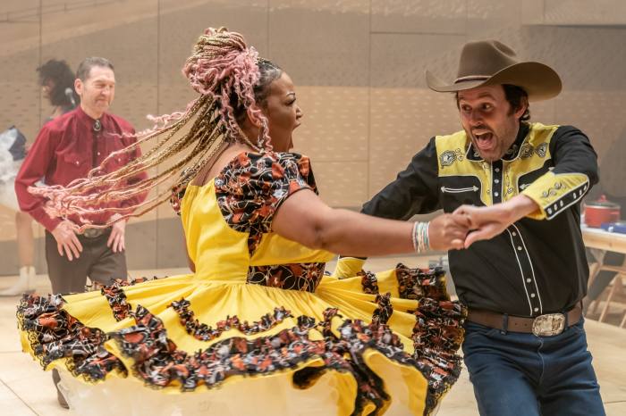 A woman in a saloon-style dress and a man in a cowboy shirt and stetson dance vigorously