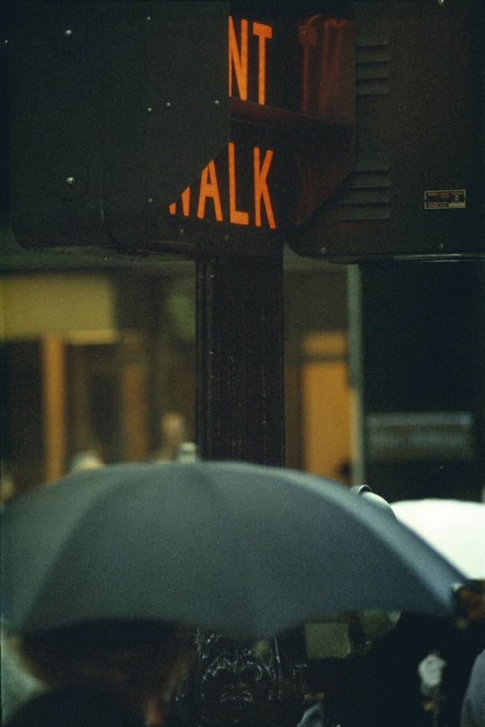 Don’t walk sign lit in red, seen above an open umbrella in gloomy light