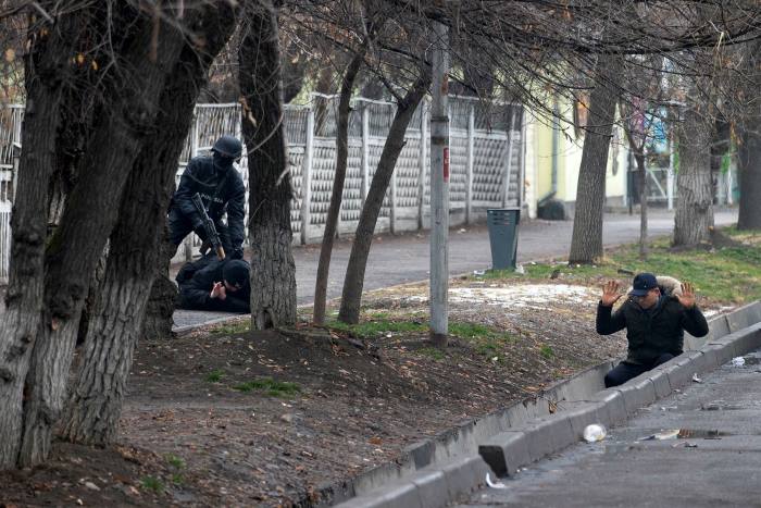 An armed police officer detains two protesters after clashes in Almaty last week
