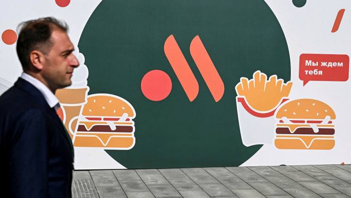 An employee stands in front of the new logo of the Russian version of a former McDonald’s restaurant before the opening ceremony