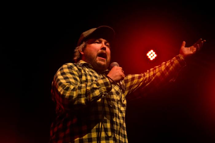 A man in a plaid shirt yells into a microphone
