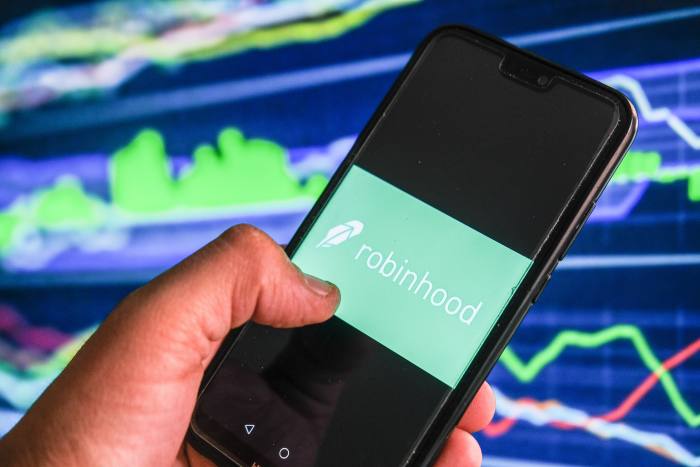 a Robinhood logo is displayed on a smartphone with stock market percentages in the background