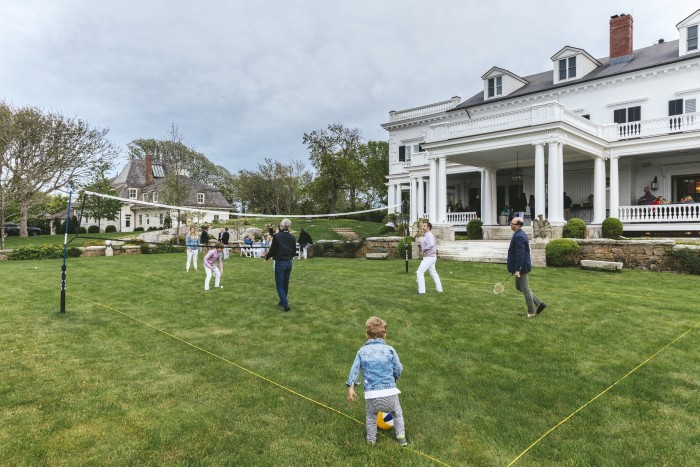 Friends and family play badminton on a Newport lawn during an early-evening get-together