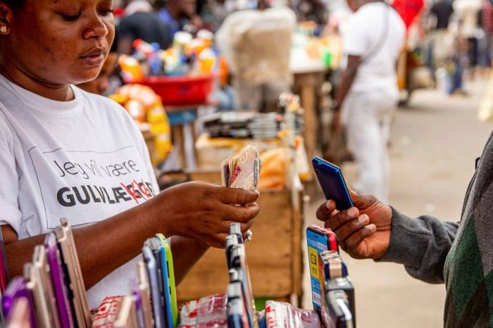 A vendor counts Nigerian naira banknotes for the purchase of a second-hand mobile phone at a market stall in Ikeja Computer Village in Lagos, Nigeria