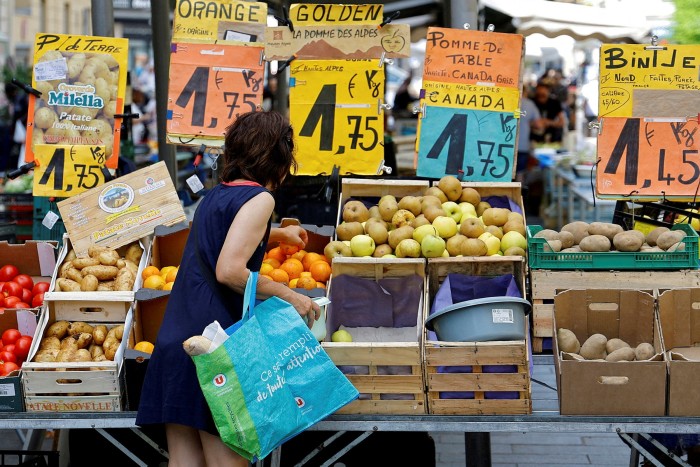 A woman shops at French food market where prices are displayed on big signs above the produce