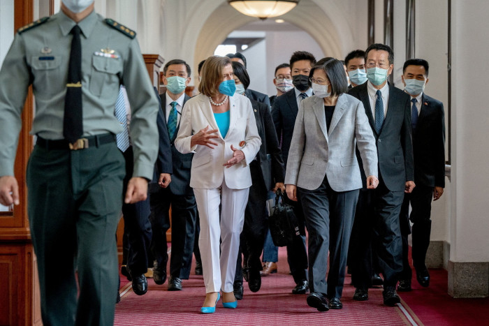 Nancy Pelosi and Tsai Ing-wen walk down a corridor surrounded by their entourages and security, all wearing face masks