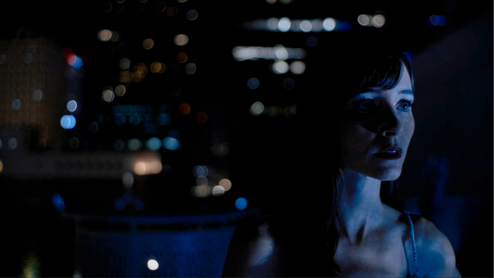 In a nocturnal scene with city lights as a backdrop, a young woman looks concerned