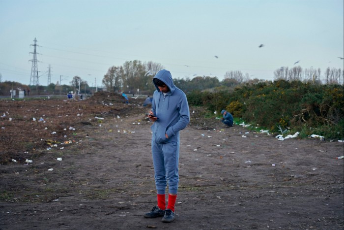 A man in a blue tracksuit stands on a desolate track, looking down at his phone