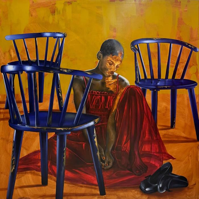 A young black woman in a red dress with her shoes off sits between three blue chairs