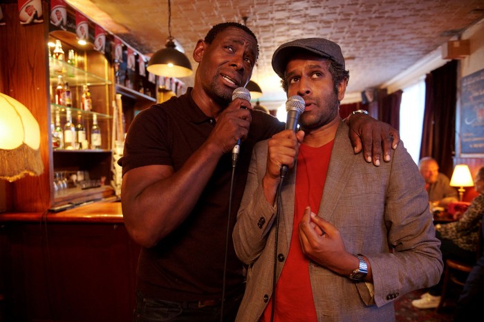 Two men hold microphones as if singing karaoke in a bar