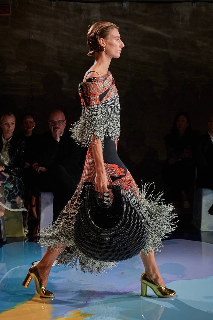 A model walks around in a fringed outfit with a fringed bag