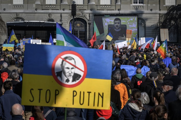 Penunjuk perasaan memegang sepanduk kuning dan biru bertulis 'Hentikan Putin' 